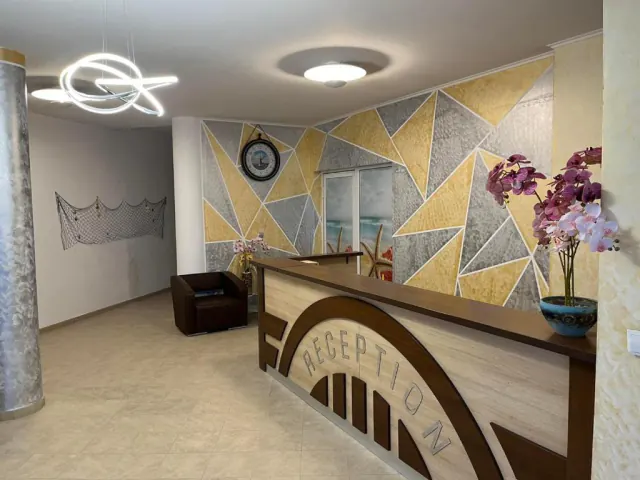 Recepce se šedo-zlatou geometrickou stěnou, hodinami a orchidejemi