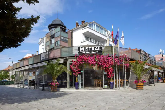 Кутова будівля з написом Mistral Restaurant, рожевою бугенвілією над входом і пальмами у вазонах