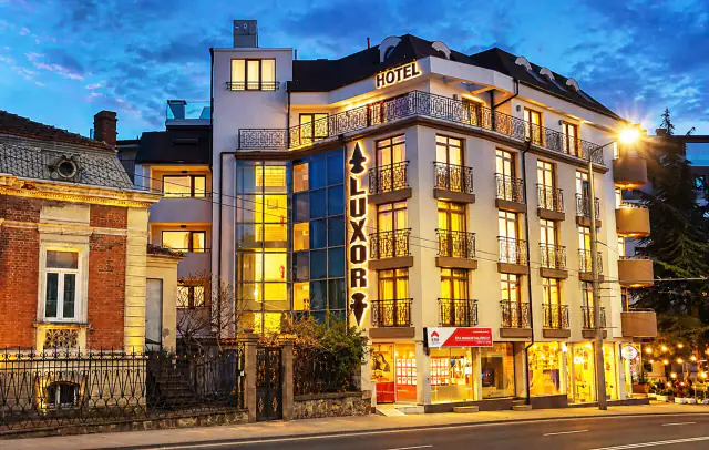 Hotel Luxor za soumraku s osvětleným proskleným schodištěm.