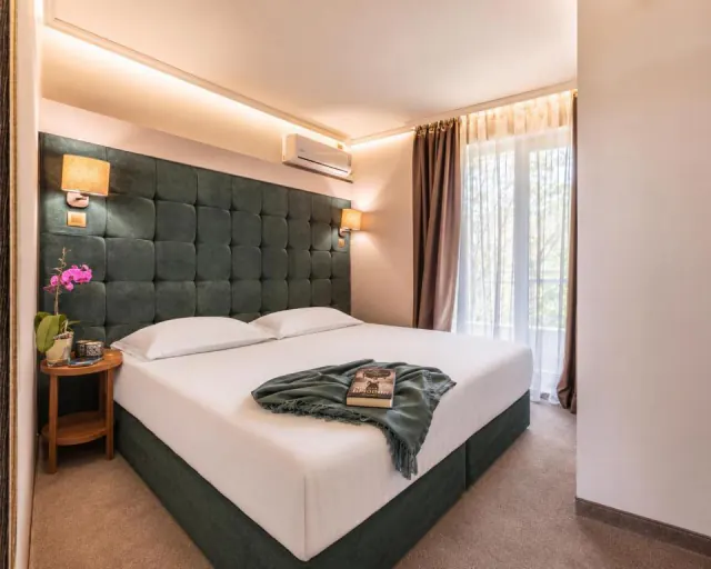 Dvoulůžkový pokoj v hotelu Mikado s čalouněným zeleným čelem postele a oknem se závěsy.
