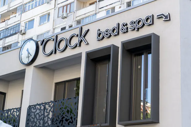 Fasáda O'Clock Bed & S.P.A. s nápisem hotelu a velkými hodinami.