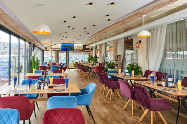 Hotelová restaurace s barevnými sametovými židlemi a prosklenou fasádou.