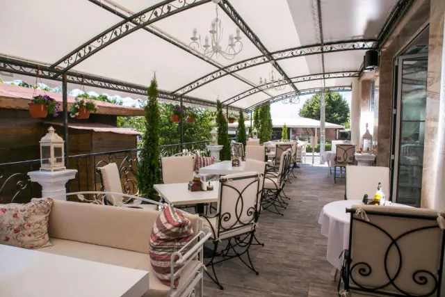 Krytá terasa restaurace s kovanými židlemi, lustry a cypřiši