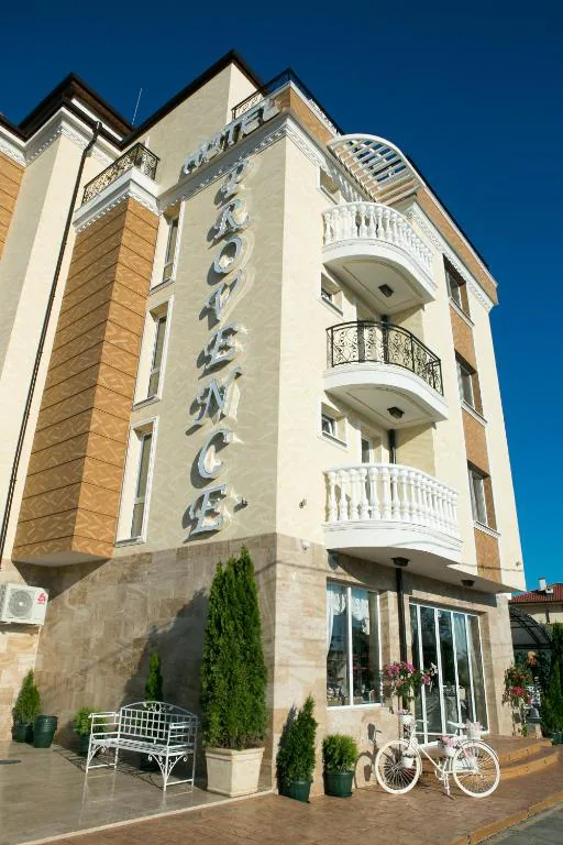 Vchod do hotelu s nápisem „Hotel Provence“ na fasádě, bílou lavičkou a dekorativním jízdním kolem