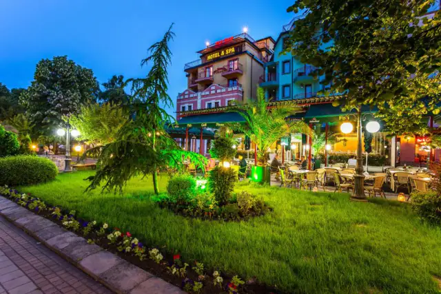 Hotel a terasa restaurace večer, s osvětlenou zahradou v popředí.