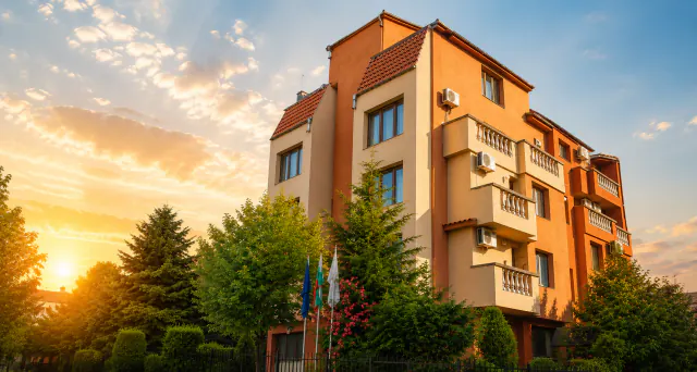 Budova rodinného hotelu Sveti Ilija při západu slunce, s balkony a se stromy před ní.