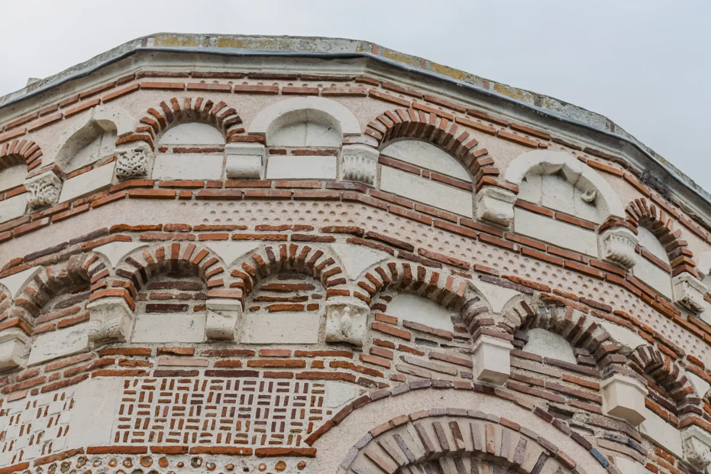 Zbliżenie górnej części apsydy — dwa rzędy nisz arkaturowych, ceglane ornamenty i wmurowane ceramiczne miseczki
