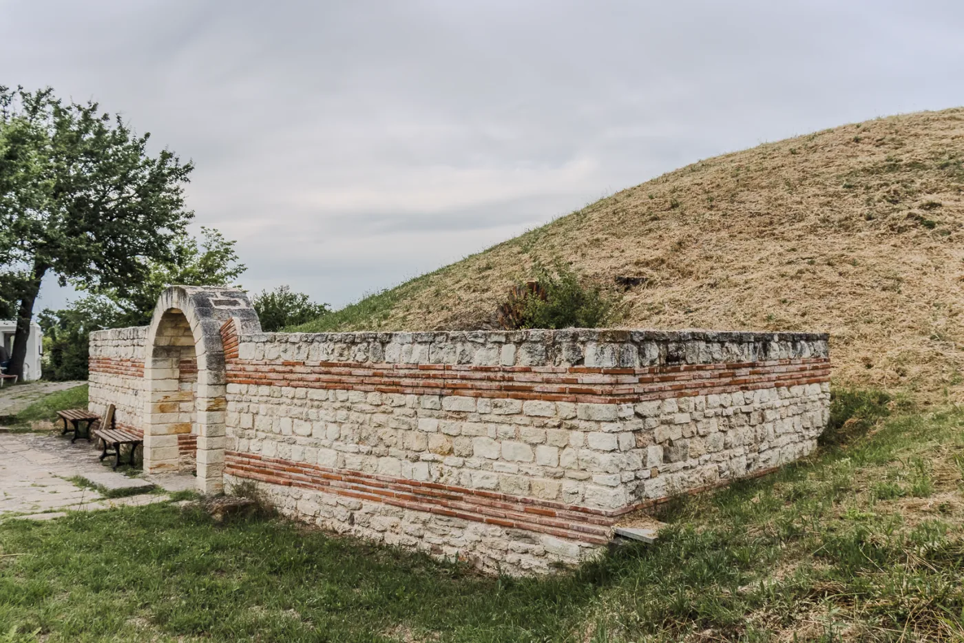 Каменно-кирпичная подпорная стена и поросшая травой насыпь могилы античной купольной гробницы близ Поморие.