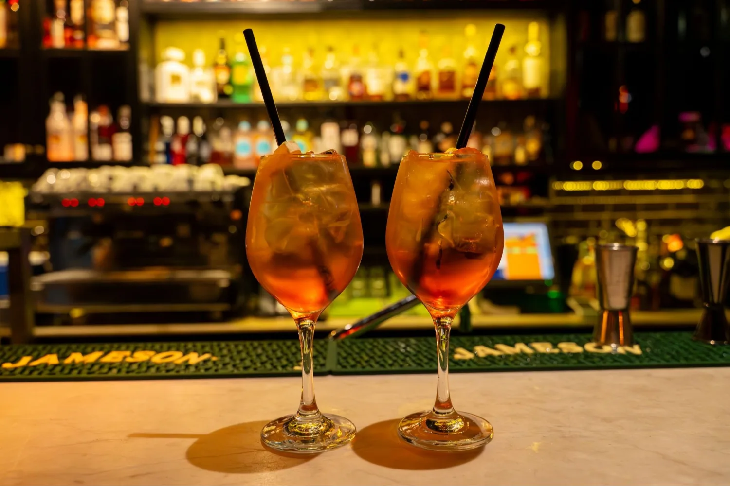 Două cocktailuri pe bar la Esco Bar, cu un raft de sticle iluminat în fundal