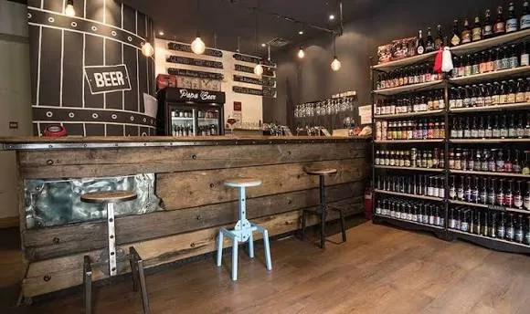 Interiorul Papa Beer — un bar de lemn și rafturi pline cu sticle de bere artizanală în localul de pe strada Milin Kamak din Burgas.